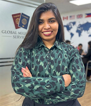 A professional portrait of Yofa Muhaima Khan smiling with arms crossed, set against a blurred corporate immigration office background featuring a world map and passport icons.